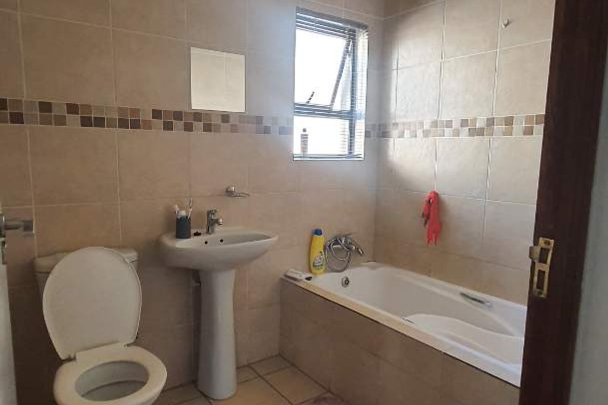 A functional bathroom featuring a pedestal basin, toilet, and built-in bathtub with neutral wall and floor tiling.
