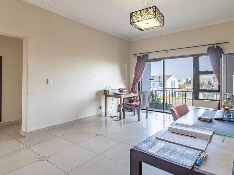 A living area featuring tiled flooring, a decorative pendant light, and a sliding glass door providing access to an outdoor balcony.