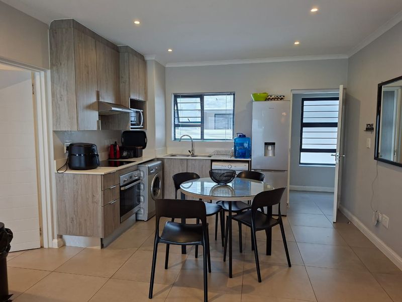Modern open-plan kitchen and dining area featuring contemporary cabinetry, integrated appliances, tiled flooring, and recessed lighting in a well-maintained apartment setting.