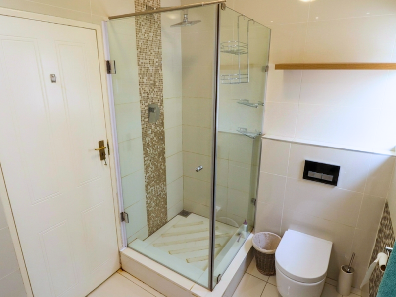 Modern bathroom featuring a glass-enclosed shower with a rain shower head, wall-mounted toilet, and elegant mosaic tile accents.