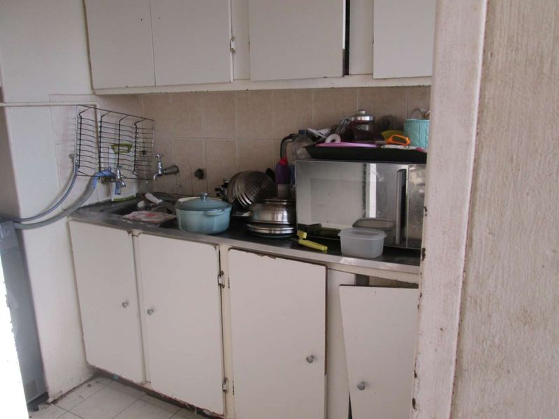 A compact kitchen area featuring built-in cabinetry, a stainless steel sink, and tiled backsplash, currently showing significant signs of wear and damage.