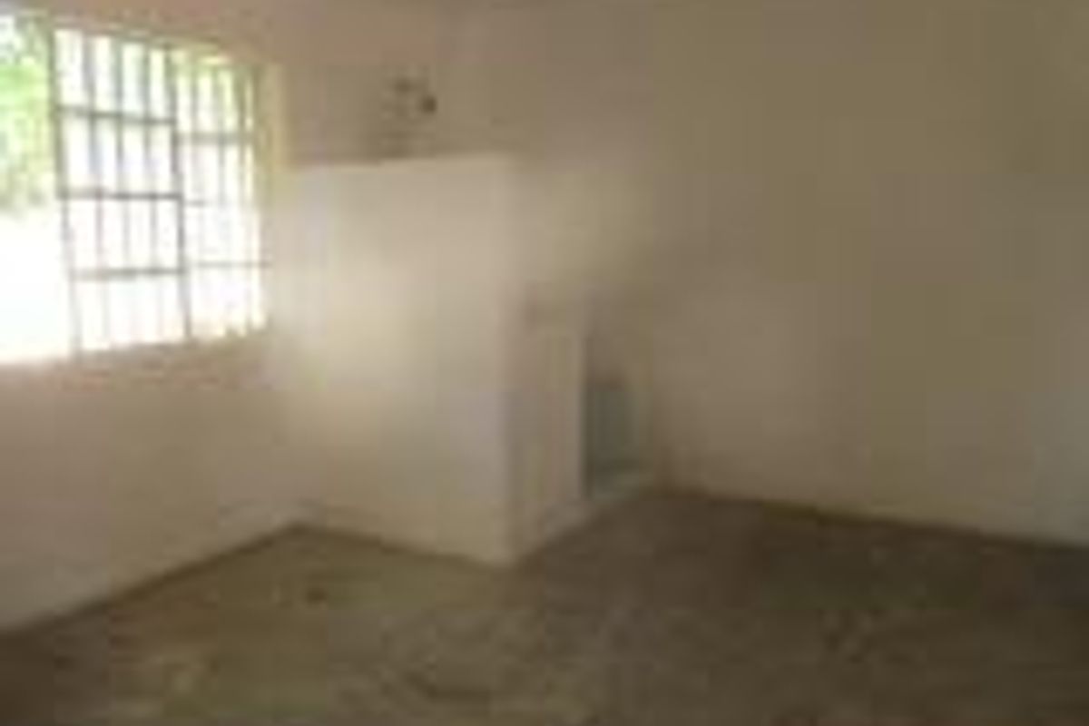 A basic, unfinished interior space featuring a concrete floor, a simple partition wall, and a window with security bars.
