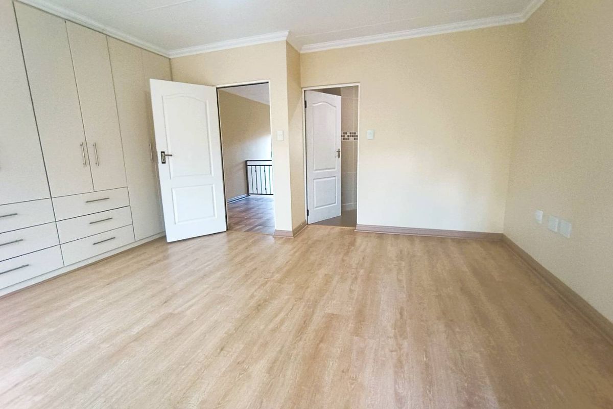 A spacious bedroom featuring light wood-look laminate flooring, built-in cabinetry, and access to an adjoining room and bathroom.