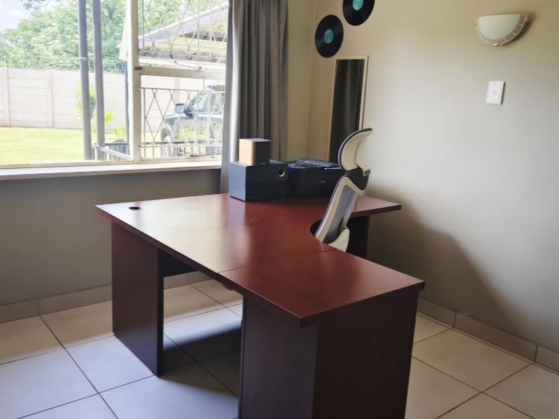 A functional home office space featuring tiled flooring, a large window with security bars, and neutral wall finishes.