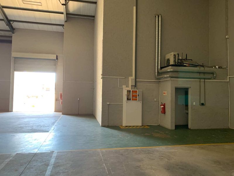 Spacious industrial warehouse unit featuring high ceilings, exposed steel trusses, a large roller shutter door, and durable epoxy-coated flooring.