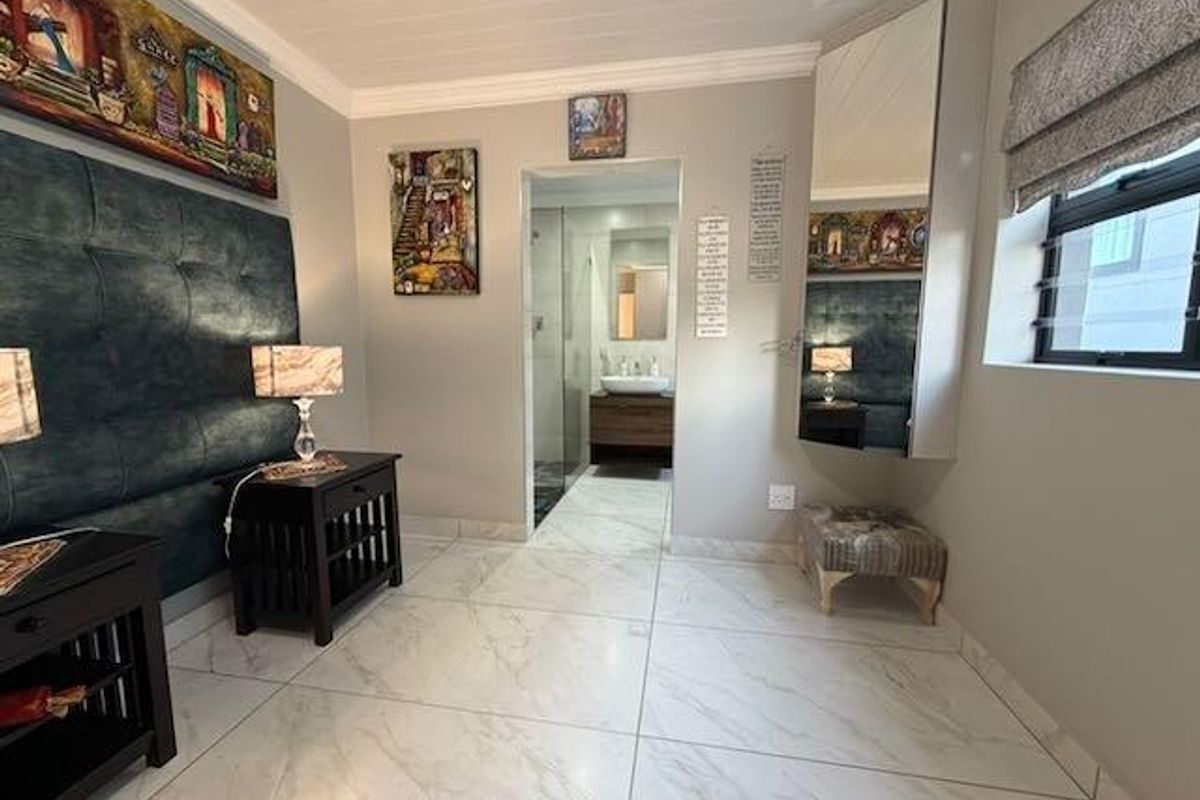 A well-maintained bedroom featuring large-format marble-look floor tiles, a built-in mirrored vanity unit, and direct access to an en-suite bathroom.