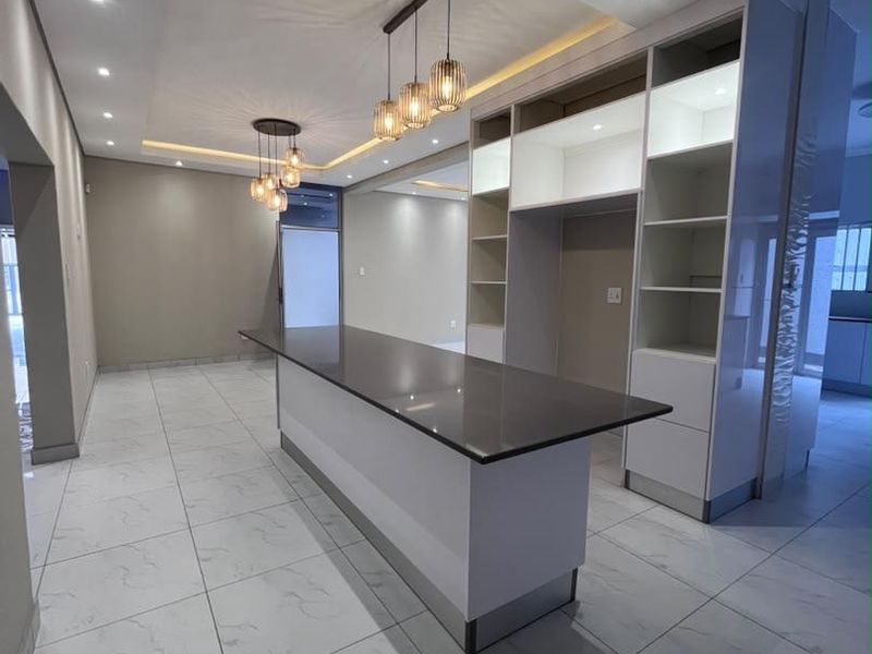 Modern kitchen area featuring a large island with quartz countertop, custom built-in cabinetry, recessed lighting, and elegant pendant fixtures over a tiled floor.