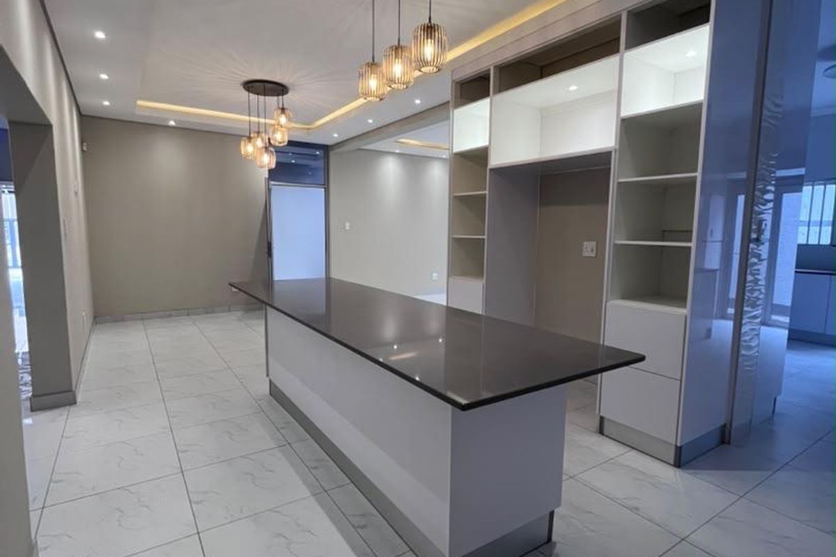 Modern kitchen area featuring a large island with quartz countertop, custom built-in cabinetry, recessed lighting, and elegant pendant fixtures over a tiled floor.