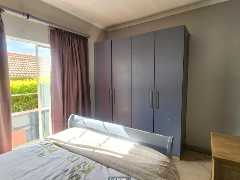 A bedroom featuring a built-in wardrobe, tiled flooring, and a large window providing natural light.