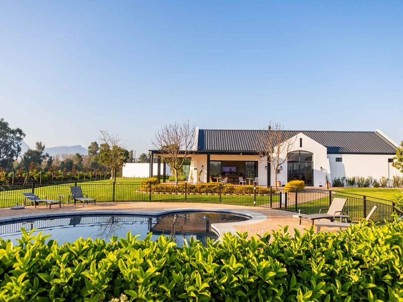 A well-maintained outdoor pool area featuring a paved deck, metal fencing, and a landscaped garden, set against a modern residential building with a covered patio.