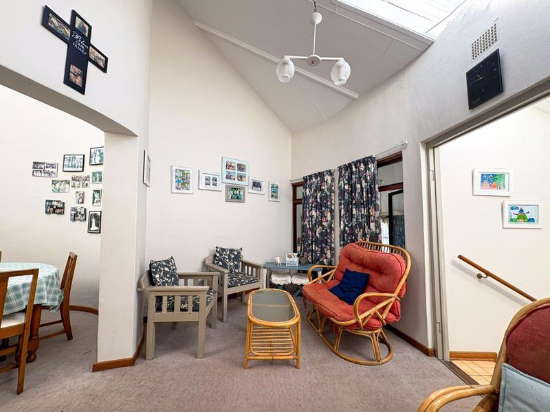 A living room featuring a high vaulted ceiling with a skylight, providing natural light, and carpeted flooring throughout the space.