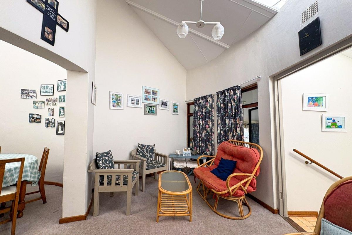 A living room featuring a high vaulted ceiling with a skylight, providing natural light, and carpeted flooring throughout the space.
