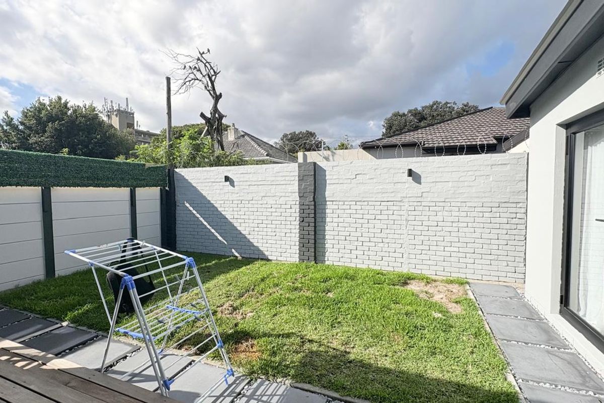 A private rear garden featuring a manicured lawn, perimeter brick boundary walls with security spikes, and paved pathways leading to the main dwelling.