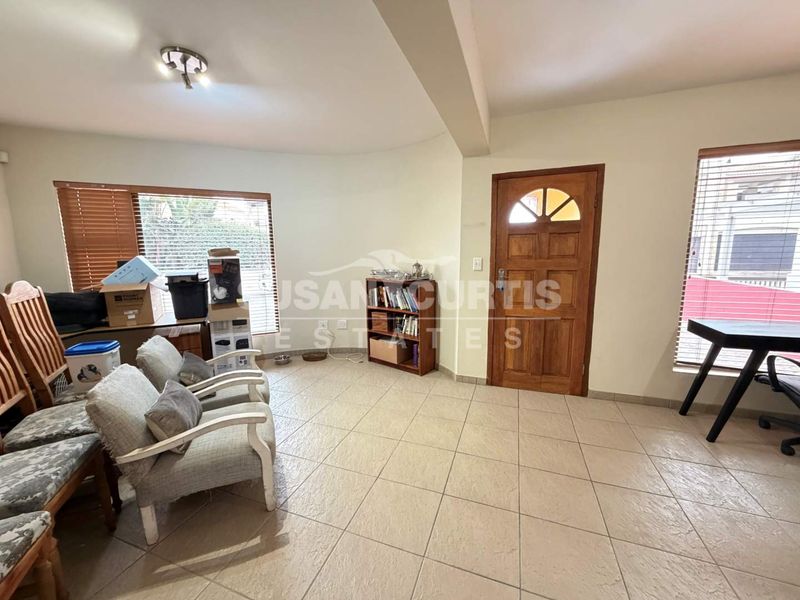 A living area featuring tiled flooring, a wooden front door, and large windows with venetian blinds.