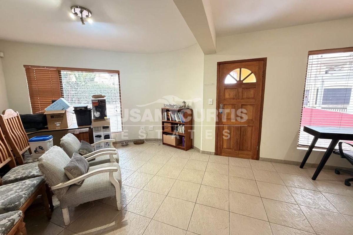 A living area featuring tiled flooring, a wooden front door, and large windows with venetian blinds.