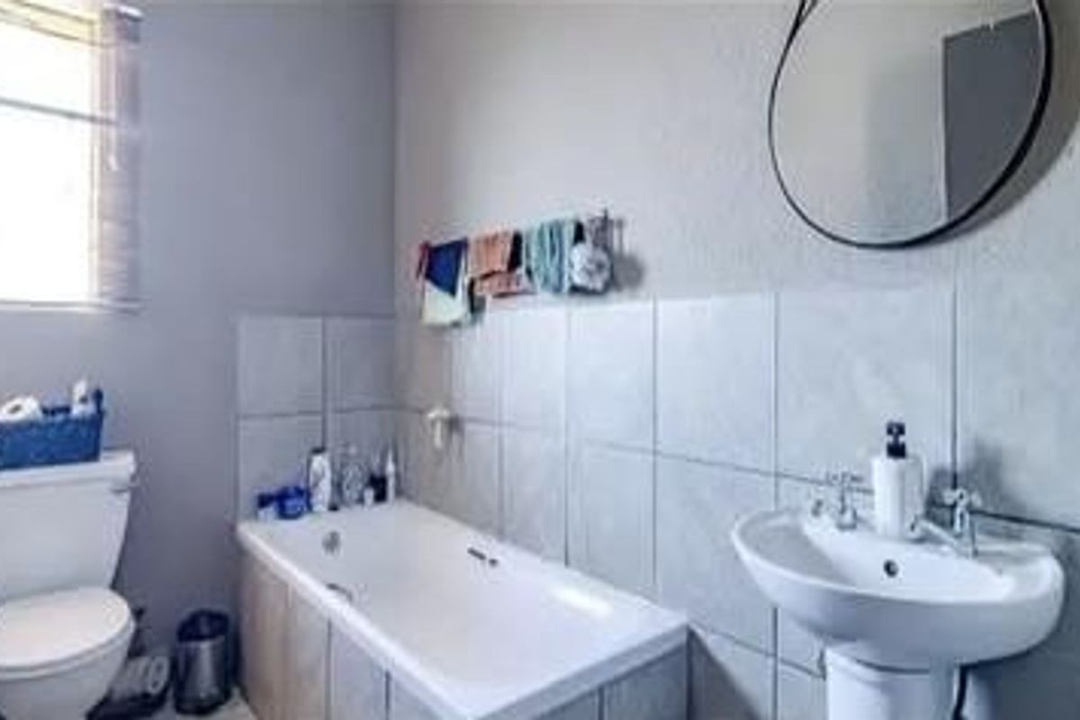 A functional bathroom featuring a standard bathtub, pedestal basin, and toilet with tiled splashbacks and a window for natural light.