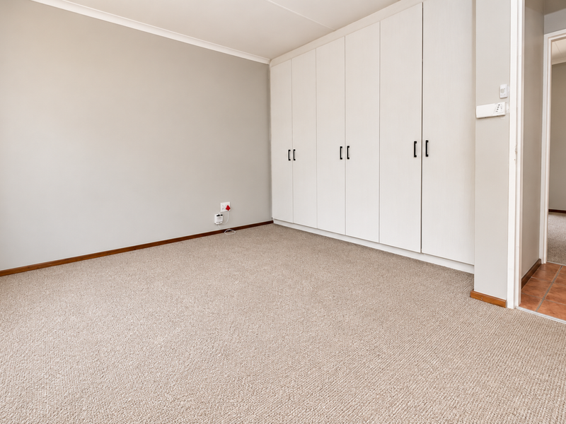 A clean, empty bedroom featuring neutral walls, carpeted flooring, and extensive built-in cupboard storage.