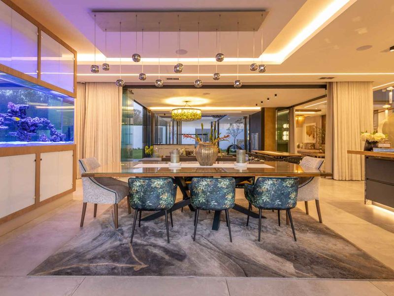 Spacious open-plan dining area featuring large format floor tiles, recessed cove lighting, and a striking built-in aquarium, seamlessly connecting to the outdoor patio.