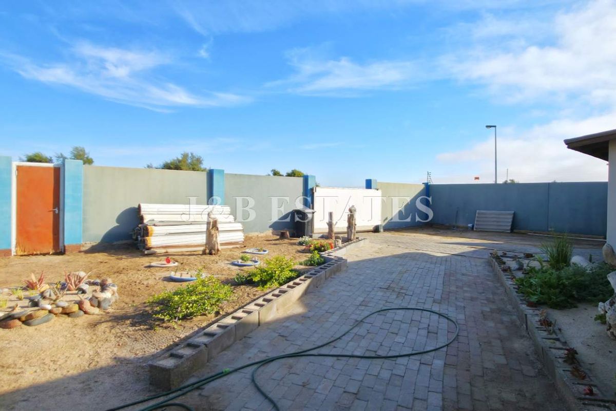 A spacious rear outdoor area featuring a paved walkway, boundary wall, and open ground space with potential for landscaping.