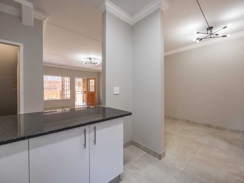 An open-plan living and kitchen area featuring neutral tiled floors, modern pendant lighting, crown molding, and a sleek kitchen counter with granite tops.
