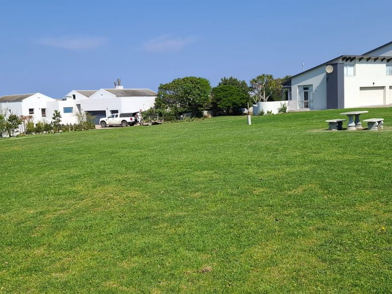A spacious, well-maintained residential lawn area featuring a concrete bench, situated within a developed neighbourhood setting.