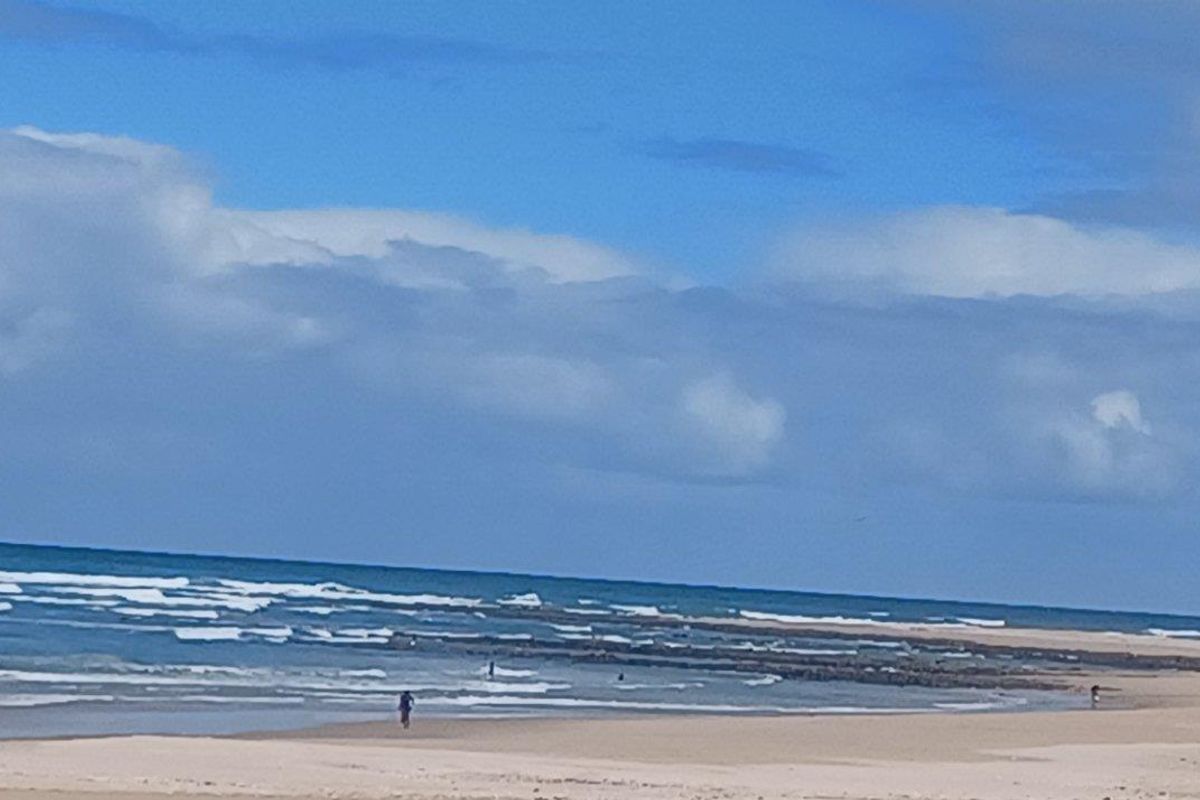 A scenic view of the coastline featuring sandy beach and ocean waves under a blue sky.