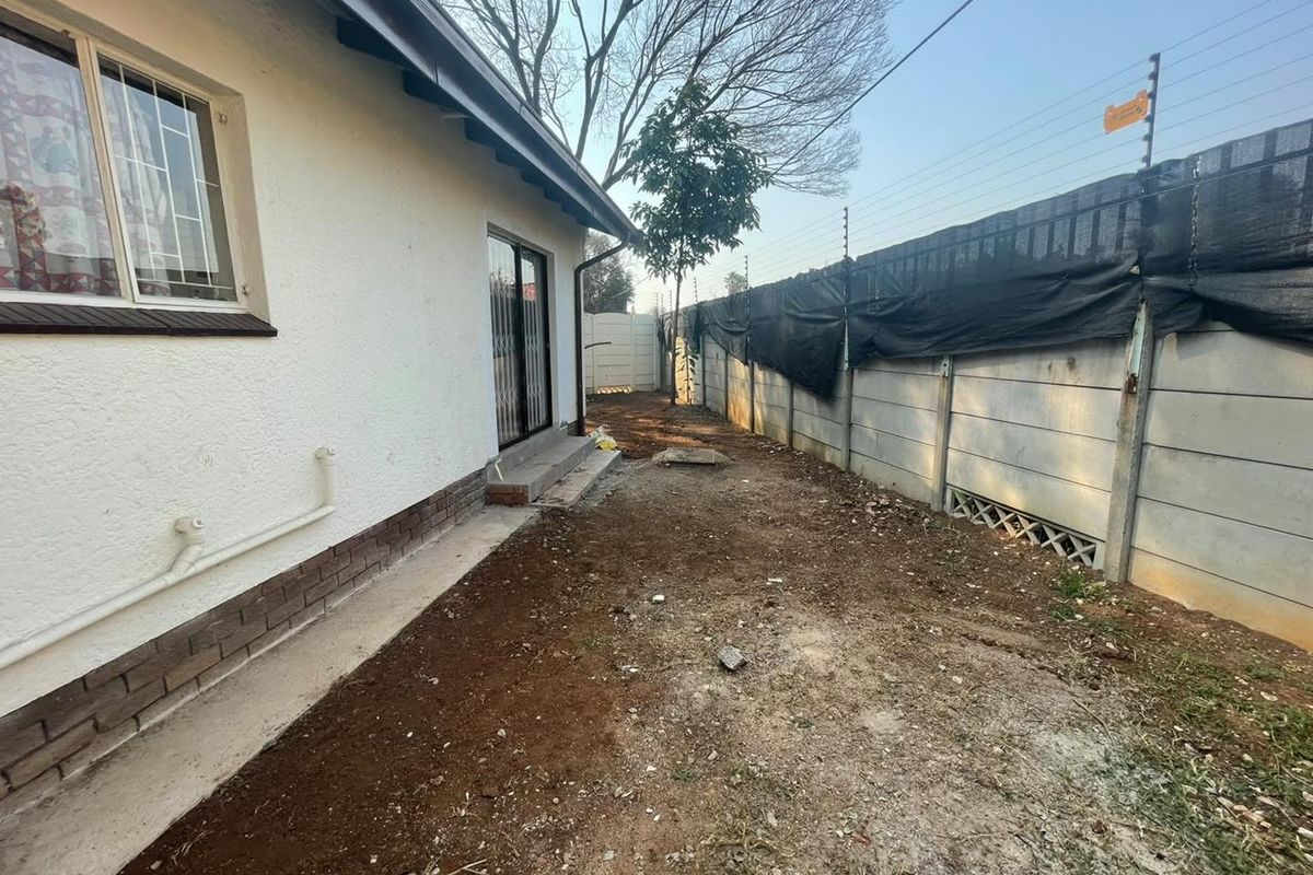 Rear exterior view of the cottage featuring a sliding door, precast boundary wall with electric fencing, and an unlandscaped garden area.