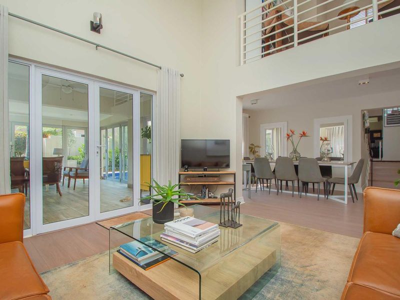 Spacious open-plan living and dining area featuring double volume ceilings, a mezzanine level with metal balustrades, and direct access to the patio.
