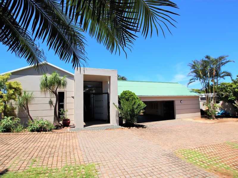 Front elevation of a single-story house featuring a paved driveway, covered entrance, and integrated double garage with a green metal roof.