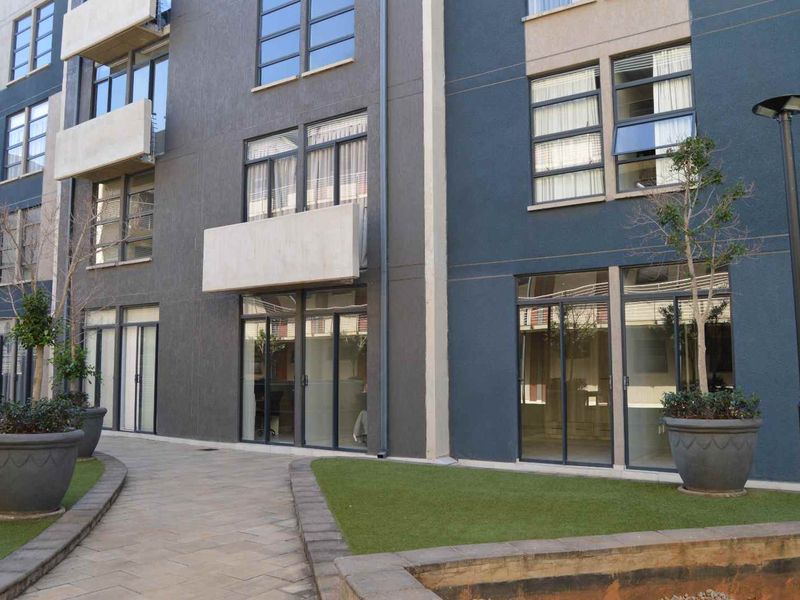 Exterior view of an apartment building featuring modern dark facade, sliding glass doors, paved walkways, and landscaped garden areas.