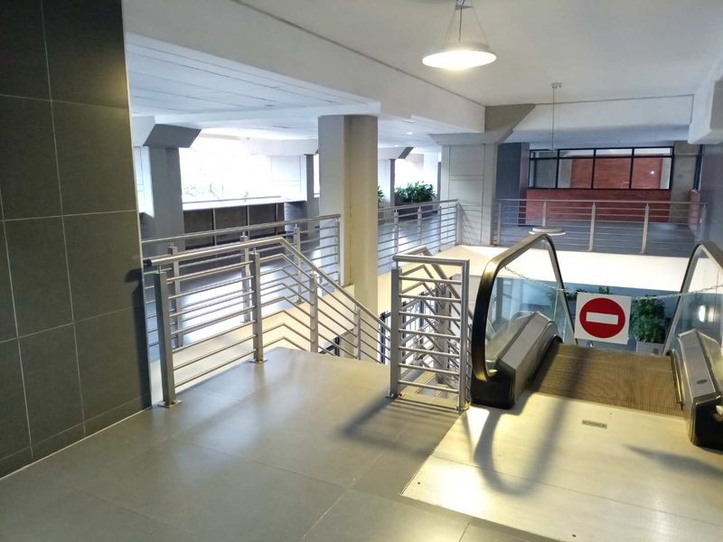 A commercial-style interior space featuring an escalator, stainless steel railings, and tiled flooring within a multi-level building structure.