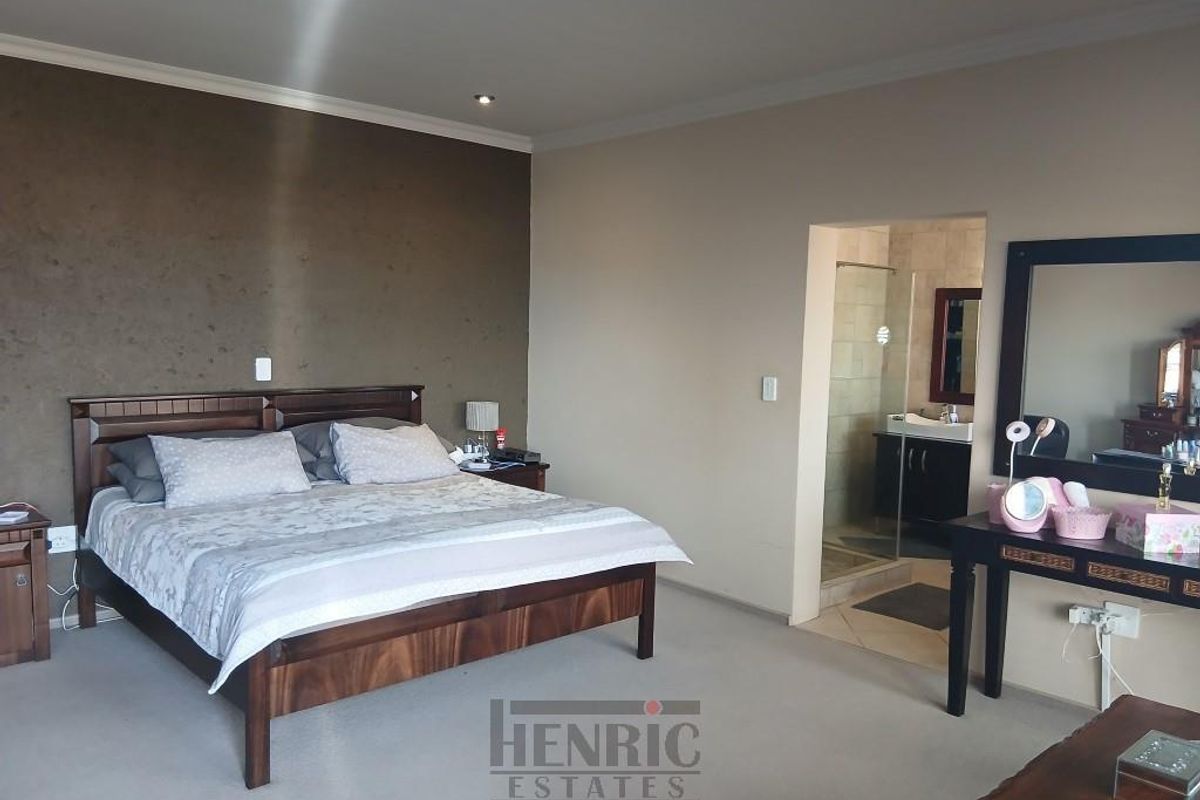 Spacious bedroom featuring a neutral color palette, an accent wall, and an adjoining en-suite bathroom with a shower.
