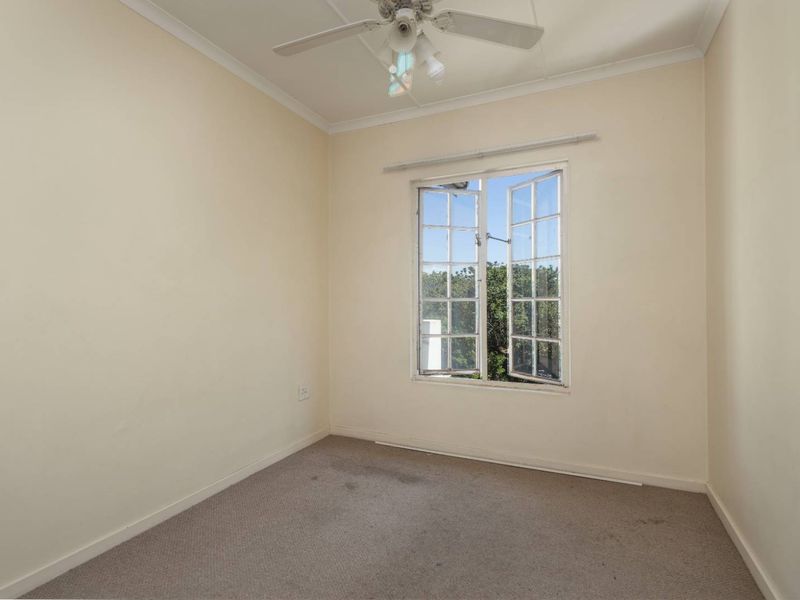 An empty bedroom featuring a ceiling fan, carpeted flooring, and a casement window providing natural light.