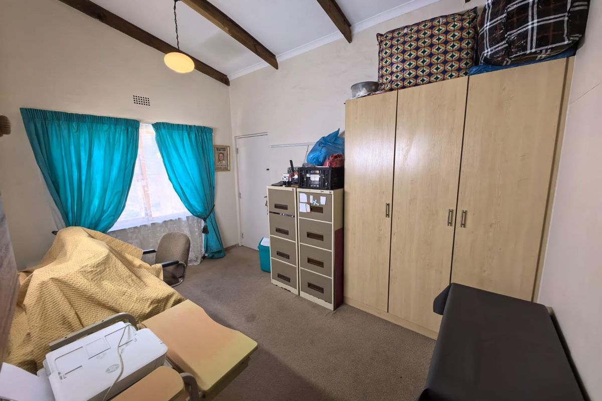 A bedroom featuring exposed timber ceiling beams, carpeted flooring, and a built-in wardrobe, offering a functional space with potential for modernization.