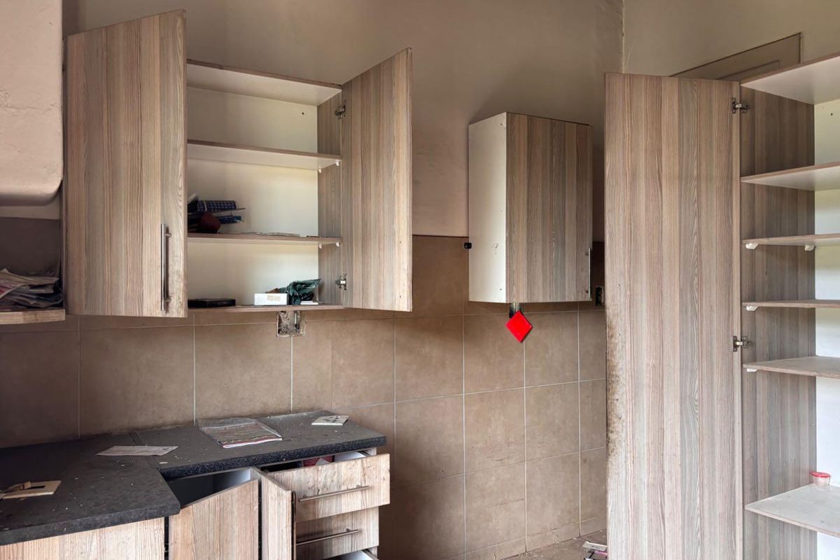 A dated kitchen area featuring wood-look laminate cabinetry, tiled splashbacks, and dark countertops, currently in need of maintenance and cosmetic updates.