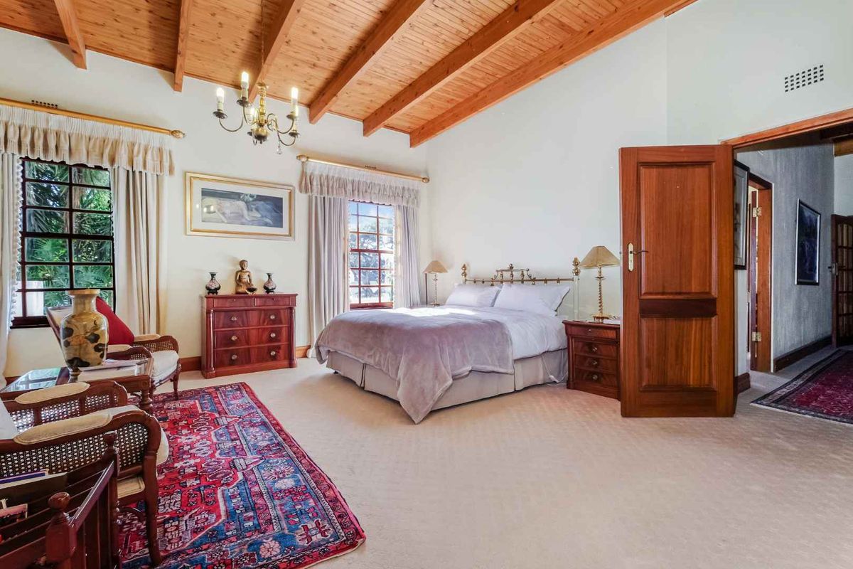 Spacious bedroom featuring exposed timber beam vaulted ceilings, neutral carpeting, and large windows allowing for ample natural light.