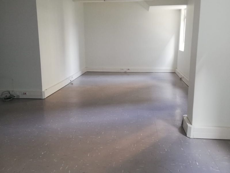 A spacious, empty office area featuring neutral white walls, durable vinyl flooring, and exposed industrial-style ceiling cable trays.