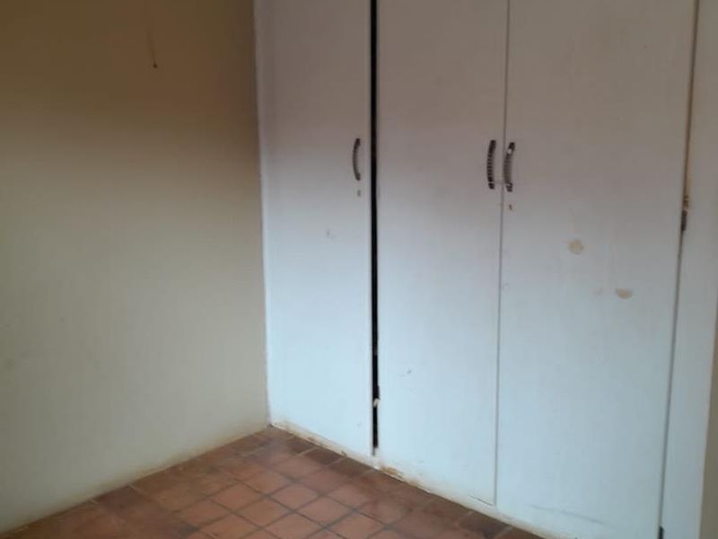 An empty bedroom featuring built-in cupboards and traditional terracotta-style floor tiles, requiring cosmetic updates to refresh the space.