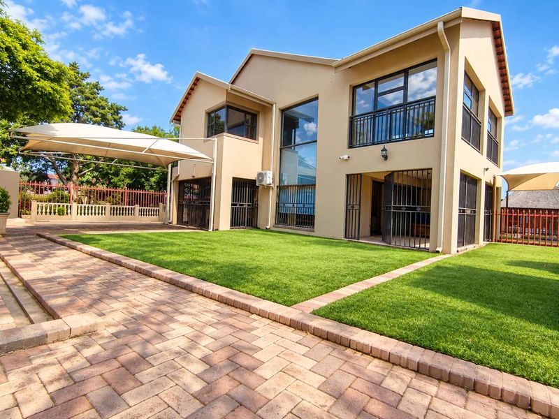 Rear view of a two-story house featuring a paved patio area, well-maintained lawn, shade sail, and secure metal gates.