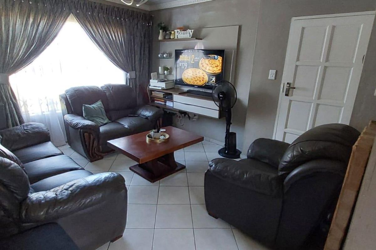 A comfortable living room featuring tiled flooring, a built-in media wall unit, and a large window with curtains.