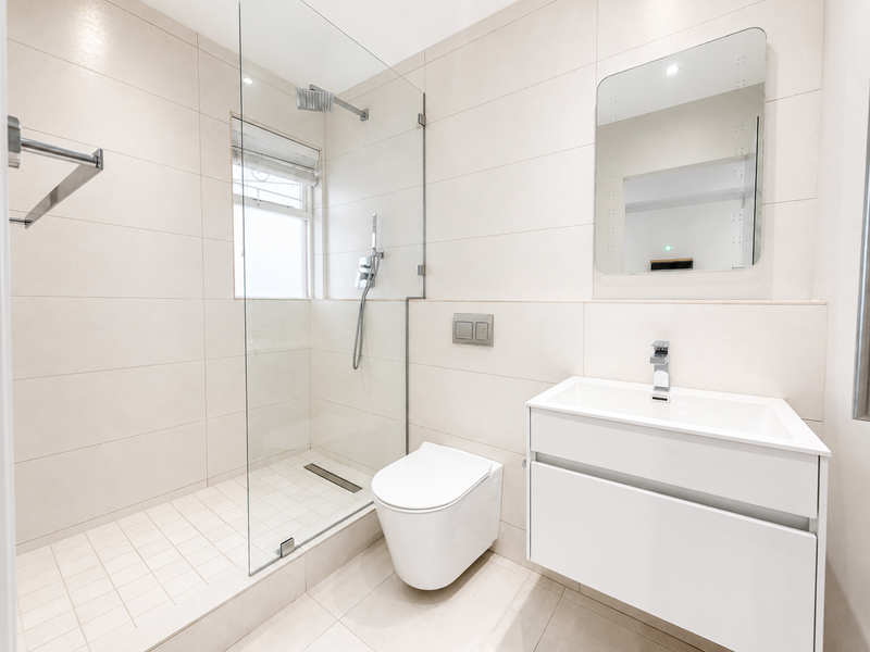 Modern, well-maintained bathroom featuring a wall-mounted vanity, walk-in shower with glass screen, and wall-mounted toilet with neutral tiled finishes.