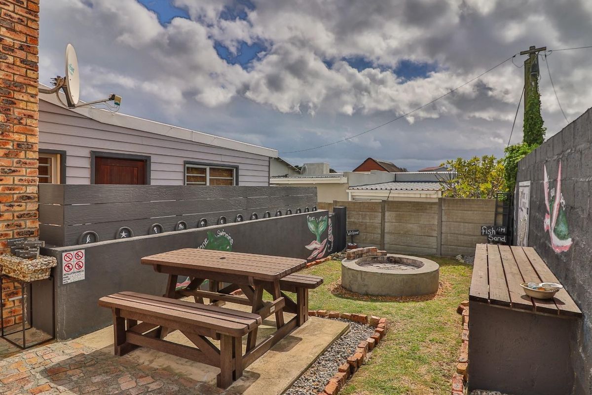A private rear garden area featuring a built-in fire pit, paved patio space, and perimeter boundary walls with decorative murals.