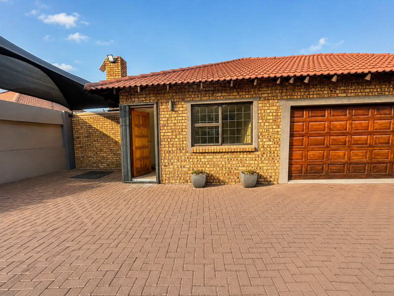 Front exterior view of a face brick house featuring a paved driveway, tiled roof, wooden garage door, and a secure entrance.