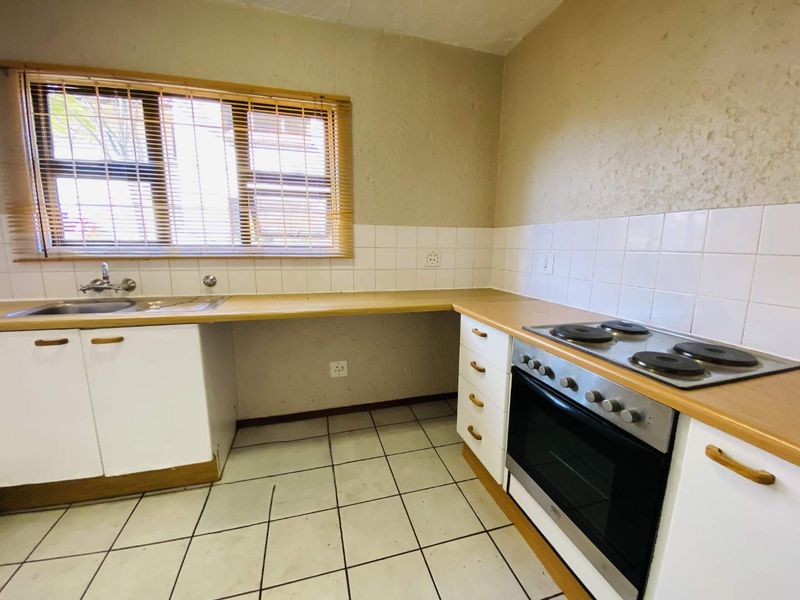 A functional kitchen featuring built-in cabinetry, a stainless steel sink, electric hob, oven, and tiled splashbacks with neutral tiled flooring.