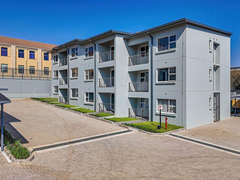 A modern multi-story apartment complex featuring paved driveway access, private balconies with metal railings, and dedicated covered parking bays.