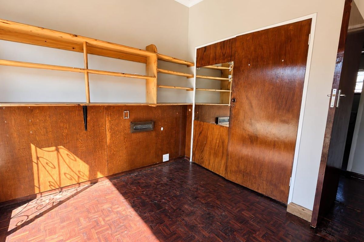 A bedroom featuring original parquet flooring, built-in wooden shelving, and a large built-in wardrobe with an integrated mirror.