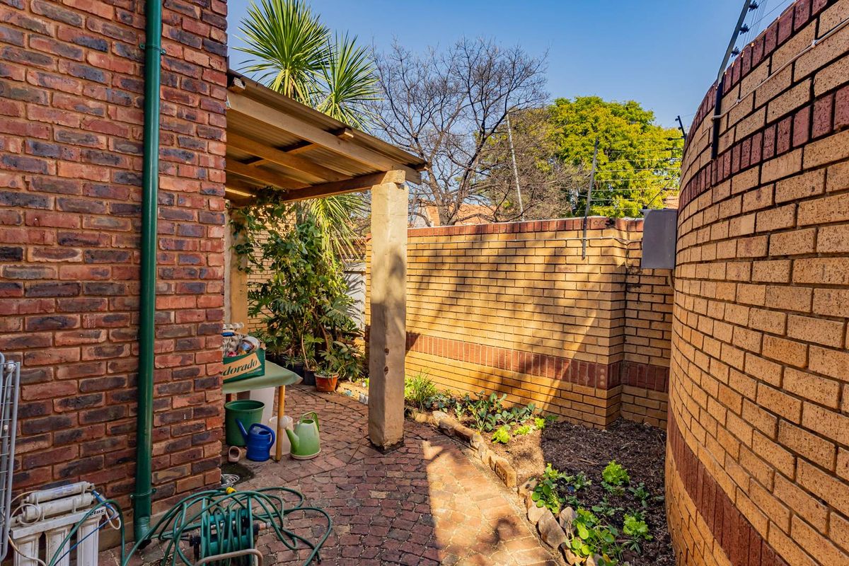 A private rear courtyard featuring brick boundary walls with electric fencing, a paved floor, and a small covered patio area.