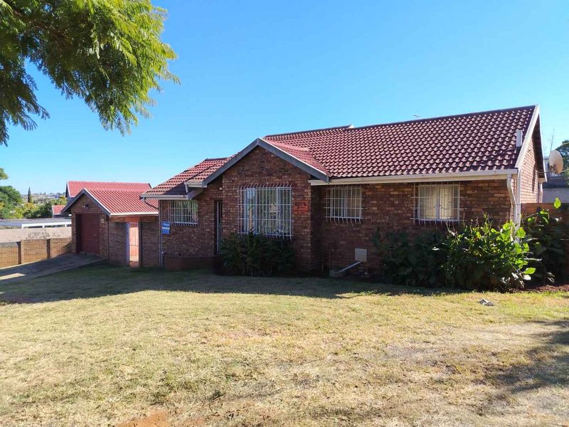 Front view of a face brick house featuring a tiled roof, security bars on windows, and an attached garage with a spacious front lawn.