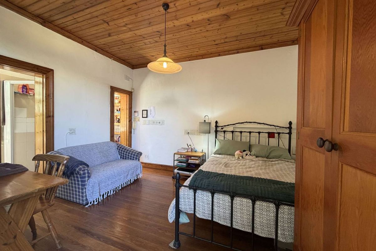 Spacious bedroom featuring warm timber ceiling and flooring, complete with a built-in wardrobe and access to adjacent rooms.