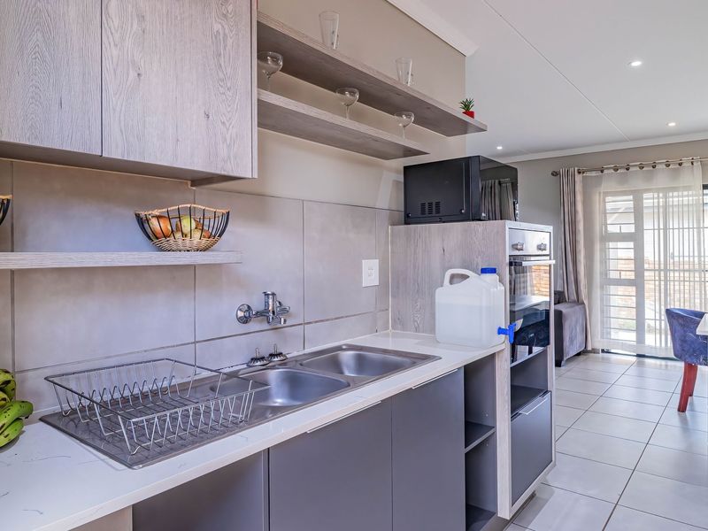 Modern open-plan kitchen featuring sleek cabinetry, stone countertops, a double sink, and built-in oven, seamlessly flowing into the adjacent living area.